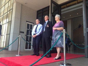 His Honour the Honourable John Hardy AO Administrator of the Northern Territory, Rowan and Mary Borella wait on the steps of Parliament House to receive the Victoria Cross.